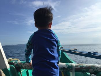 Rear view of boy standing in boat on sea