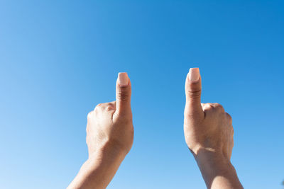 Woman's hand showing thumbs up with blue sky background