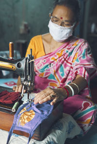 An indian housewife making handmade cloth face-masks, in a hand operated sewing machine.