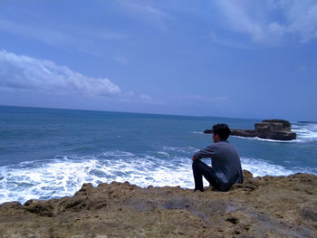 Rear view of young man sitting on rock against sea