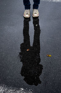 Low section of man standing on wet street with reflection