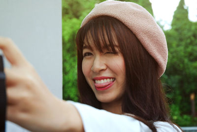 Playful woman sticking out tongue while photographing through digital camera outdoors