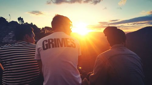 Rear view of friends sitting against sky during sunset