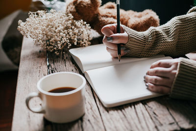 Cropped image of woman writing on book by coffee cup on table