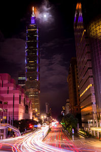 Illuminated city street and buildings against sky at night