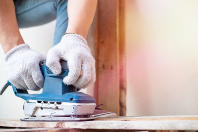 Low section of man using sander on wood