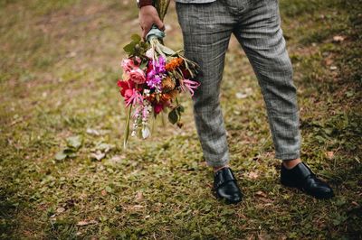 Low section of man holding bouquet while standing on grassy field