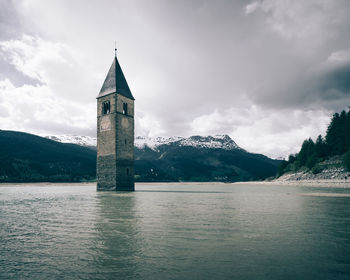 Low angle view of tower amidst lake against cloudy sky