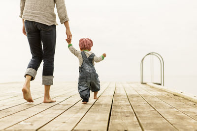 Rear view of mother walking with daughters on pier against clear sky