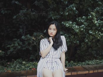 Portrait of young woman sitting against trees at park