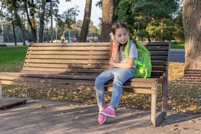 Young girl with backpack sitting on park bench in autumn afternoon