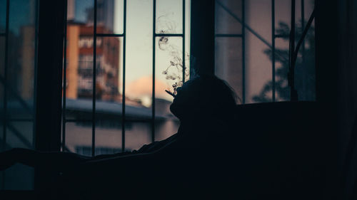 Silhouette of man smoking against window at home