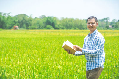 Portrait of smiling young man holding book on field