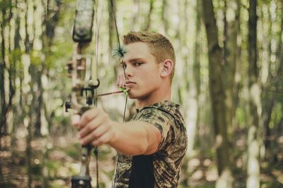 Confident man aiming with bow and arrow at forest