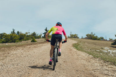 Rear view of man riding bicycle on field against sky