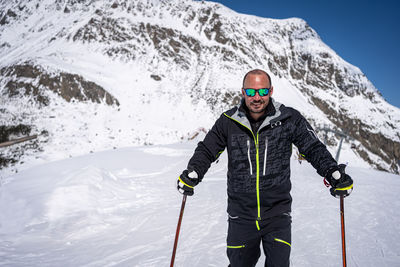 Young man with ski makes pose in mountains behind