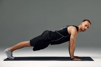 Full length of young woman exercising against black background