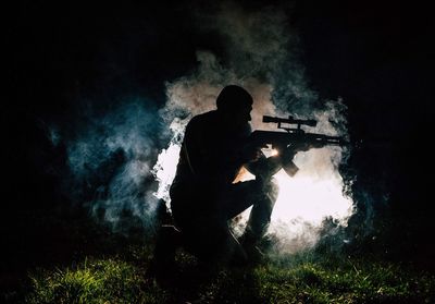 Silhouette man with weapon kneeling on field at night