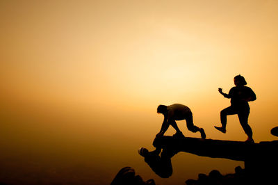 Silhouette climbers on cliff against sky during sunset