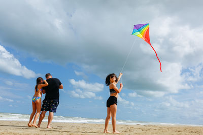Rear view of woman with arms outstretched standing at beach against sky