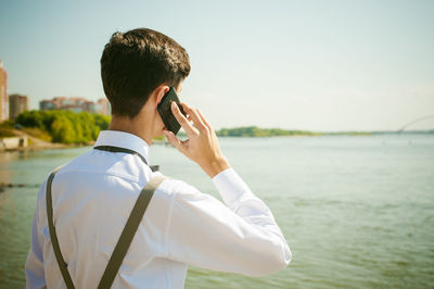 Rear view of man talking on smart phone while standing at beach