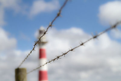 Close-up of barbed wire against lighthouse