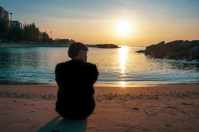 Rear view of woman looking at sea against sky during sunset