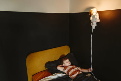 Boy turning on astronaut shape light lying on bed