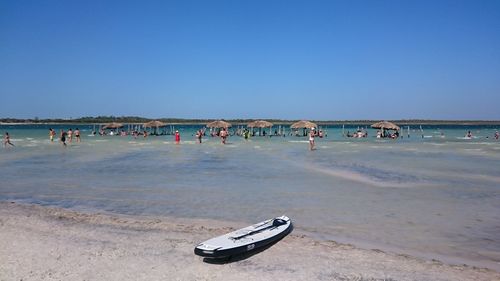 People at beach against clear blue sky