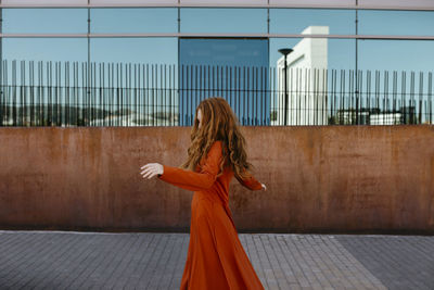 Happy young woman dancing on footpath by surrounding wall