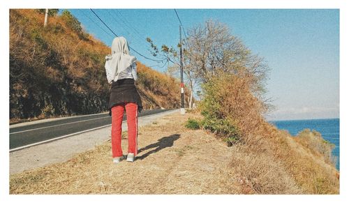 Rear view of woman standing by tree against clear sky