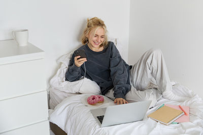 Young woman using digital tablet while lying on bed at home