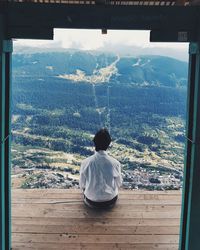 Rear view of man sitting on floorboard against mountain