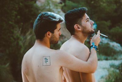 Man giving cigarette to boyfriend while standing outdoors