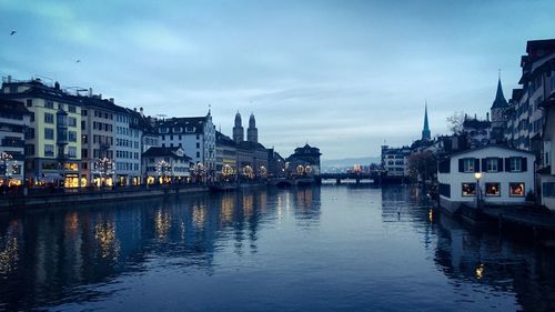 River amidst buildings against cloudy sky at dusk