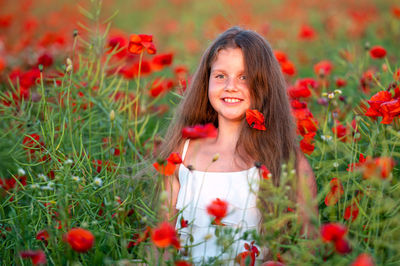 Pretty little girl wearing white dress in summer blooming poppy field walking under evening sun