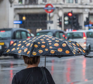 Rainy day - view from behind of a woman under a smiley umbrella in london