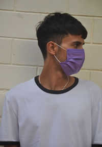 Young man wearing mask standing against wall