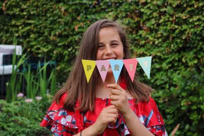 Portrait of smiling girl holding multi colored buntings against trees