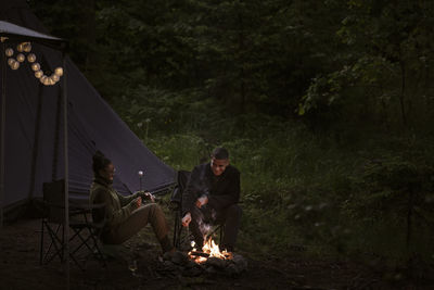 Couple camping in forest and sitting by campfire