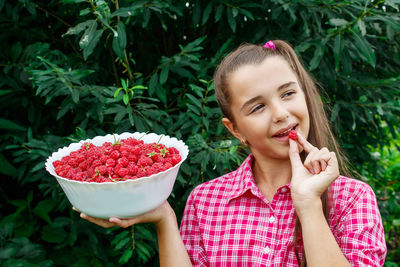 Girl holding raspberries in bowl against plants