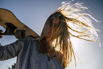 Portrait of smiling woman holding skateboard against sky