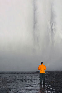 Rear view of man standing in sea against sky