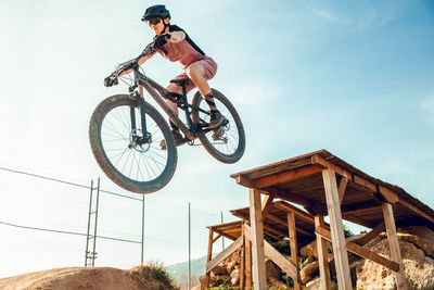 Sportswoman in black helmet and sportswear with glasses riding mountain bike jumping from a bridge in training track