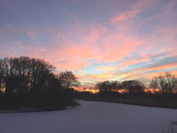 Silhouette trees on snow covered landscape against sky during sunset