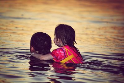 Rear view of sisters swimming in sea during sunset