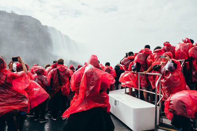 People wearing red raincoat against waterfall