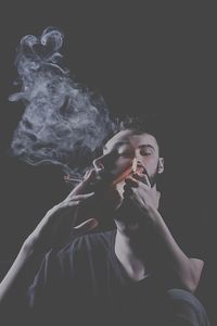 Young man smoking cigarette against black background