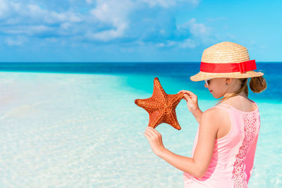 Girl holding starfish against sea