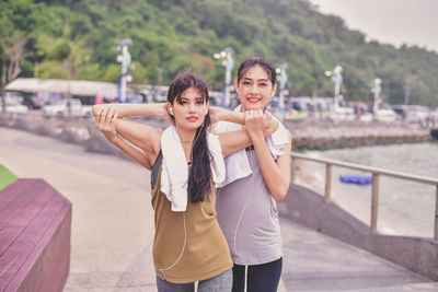 Portrait of woman assisting friend in exercising on footpath